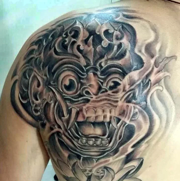 Black and grey Barong mask tattoo on a shoulder, by Demon Tattoo in Canggu, Bali