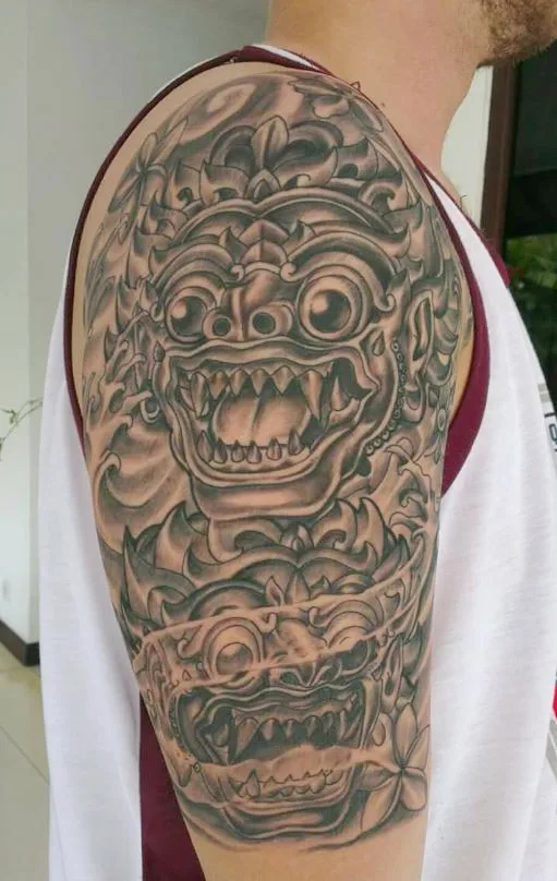Black and grey Barong mask half sleeve tattoo on an upper arm, Canggu Bali