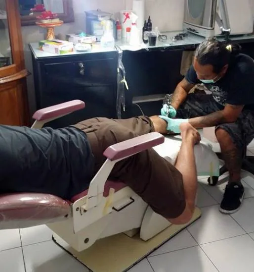 Artist in mask and gloves tattooing a client's leg on the tattoo chair