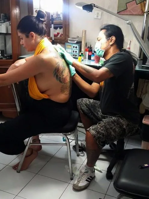 Artist wearing a mask and gloves tattooing a back piece
